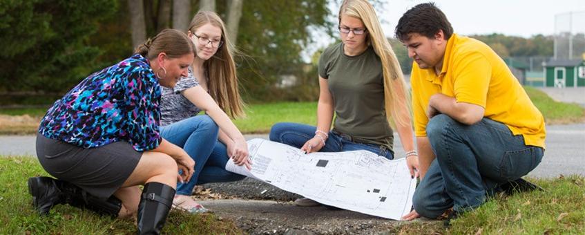 Faculty and students review blueprint schematic in the field.