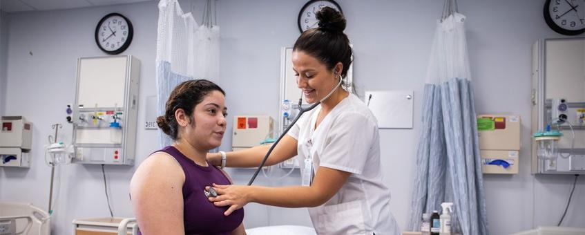 A nursing student using a stethoscope on another student.